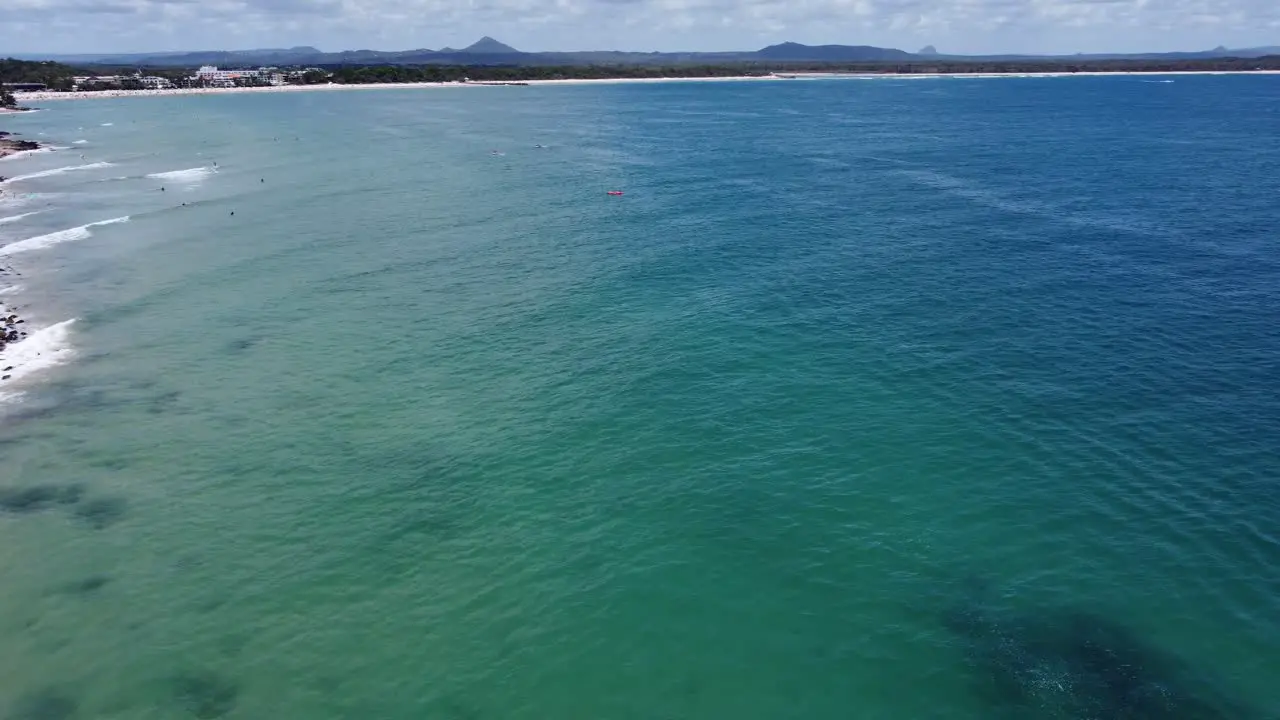 Drone flying out to sea sandy beach at the background