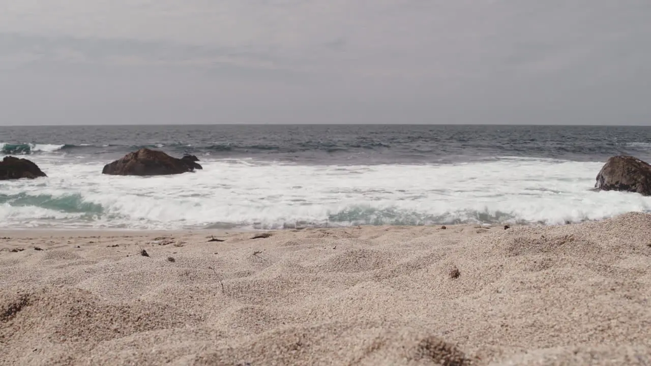 A small wave framed by three large rocks rolls ashore on a Northern California beach