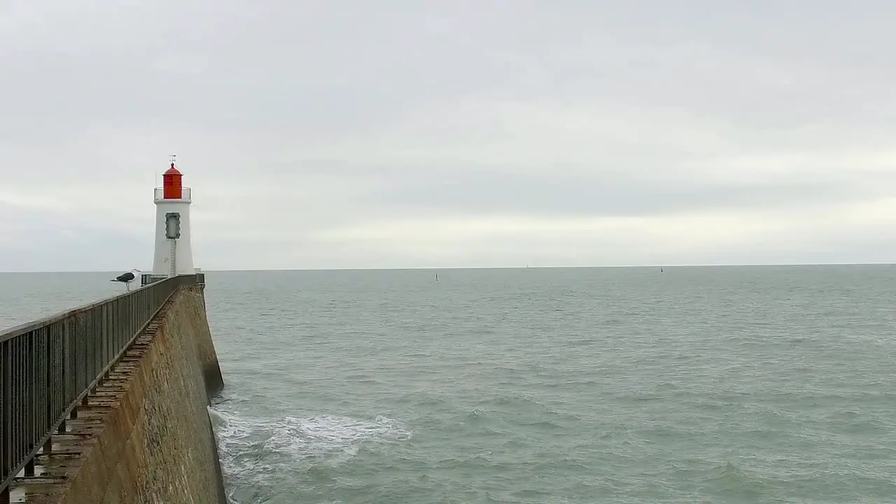 A seagull is posted on a railing in front of a red lighthouse