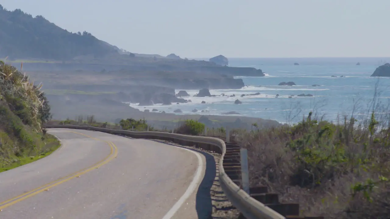 Time lapse of cars turning navigating around a bendy road with the Pacific Ocean waves cashing in the background located in Big Sur California