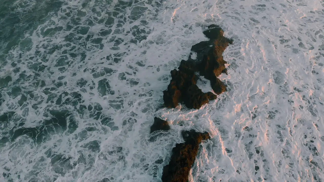 Drone footage taken of wild crashing waves on beach and rock early sunset Asia