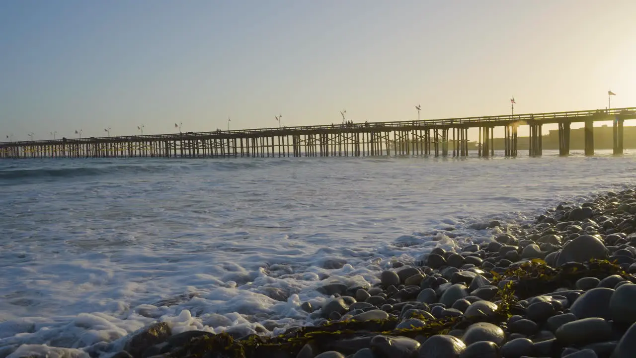 Panning shot of the Ventura Pier with sunsetting in the background while waves are crashing along the shores of Ventura Beach located in Southern California