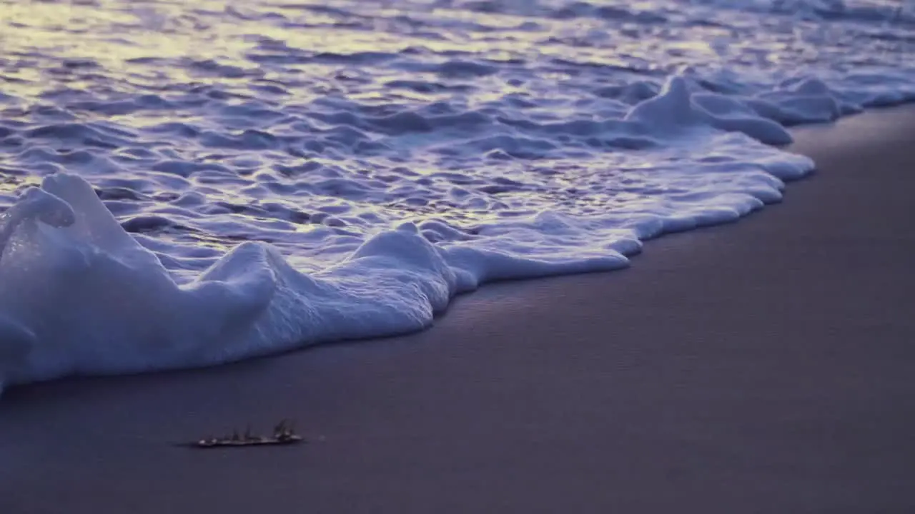 Foamy waves coming onto sandy beach during golden hour creating amazing colors in the wet sand reflection