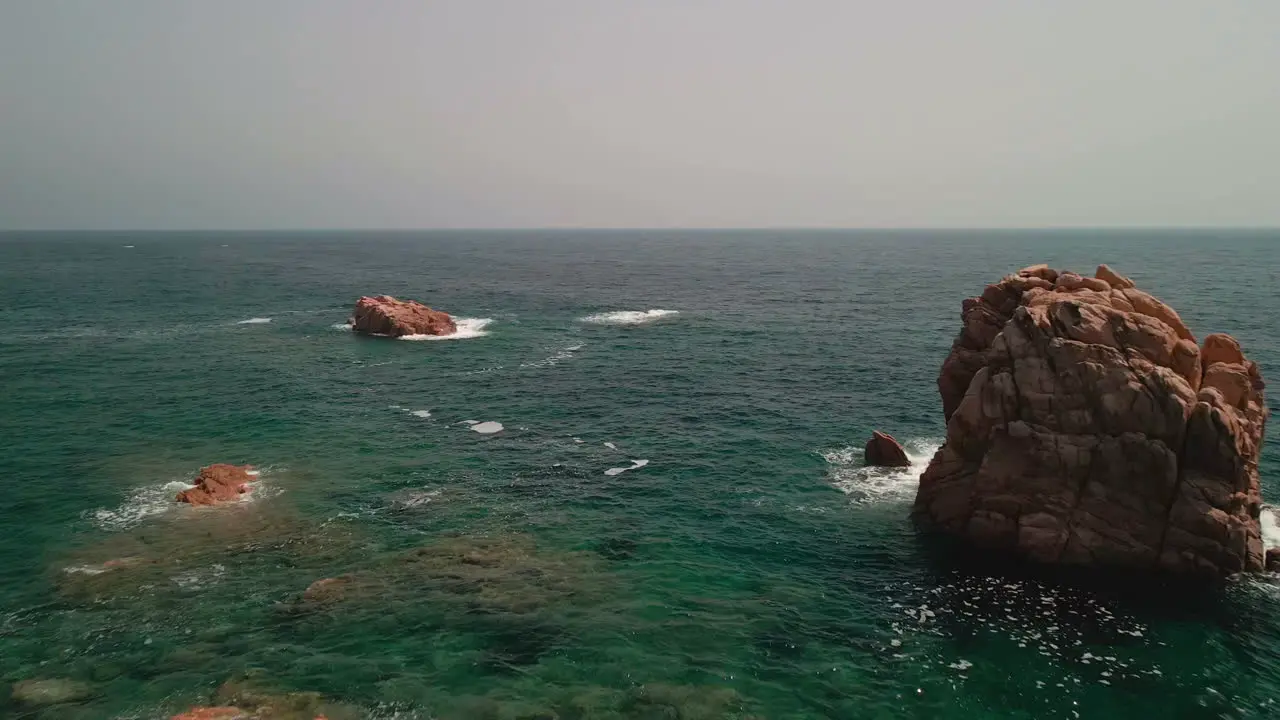 Idyllic Sea With Rocks And Breaking Waves On A Sunny Summer Day In Sardinia Italy aerial pullback