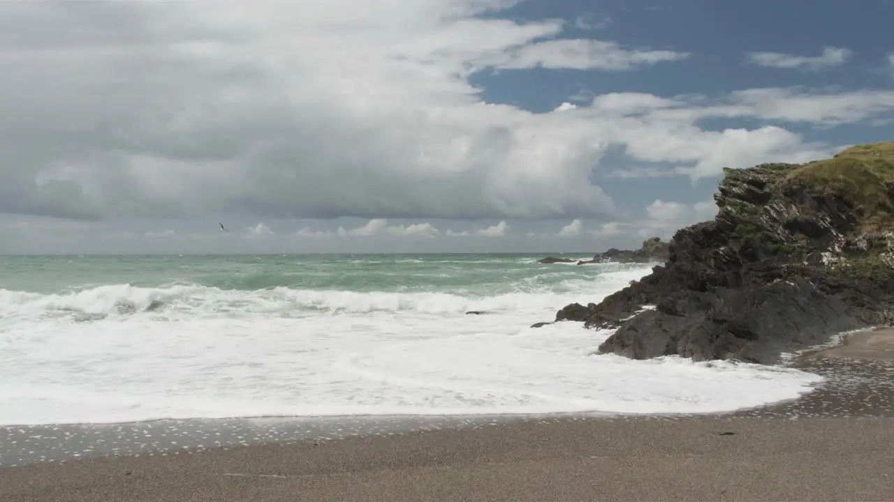 Rugged coast and crashing waves on the beach with clouds passing on a blue sky in slow motion