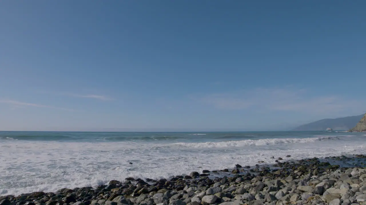 Panning shot of rocky beach and rolling waves though the Pacific Ocean located in Big Sur California