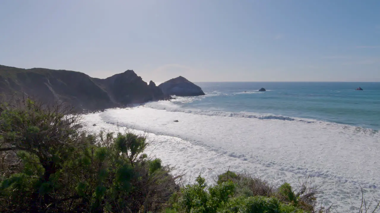 hillside view of the Pacific Ocean with rolling waves crashing along the shore on a sunny day of Big Sur California