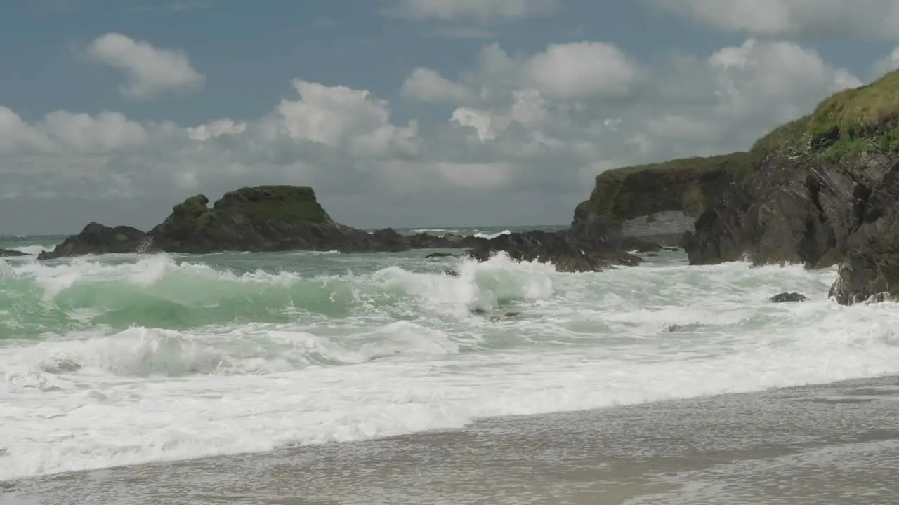 Cliffs and crashing waves on the beach with white clouds passing on a blue sky in slow motion