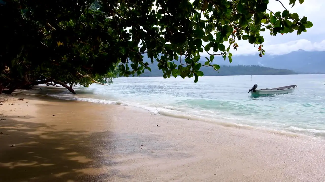 Small motorboat moored with gentle waves lapping onto beach of remote tropical island landscape in Bougainville Papua New Guinea