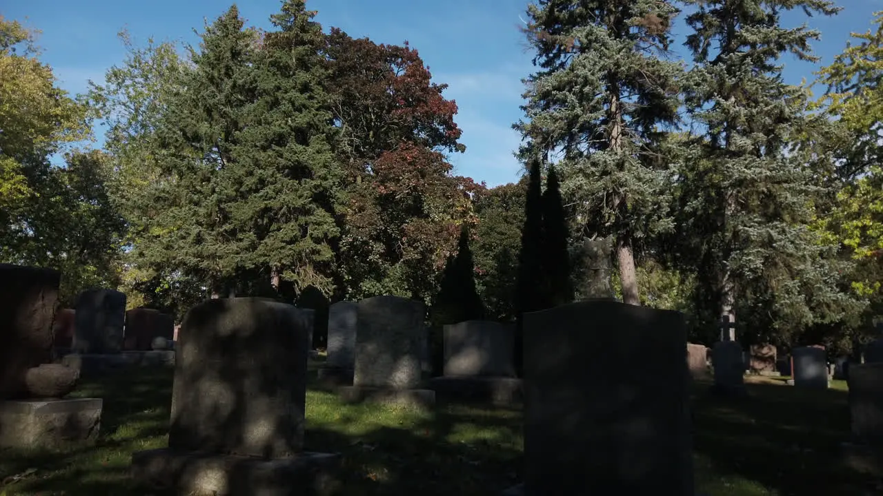 Wide daytime shot with a tilt down to empty tombstones and moving shadows