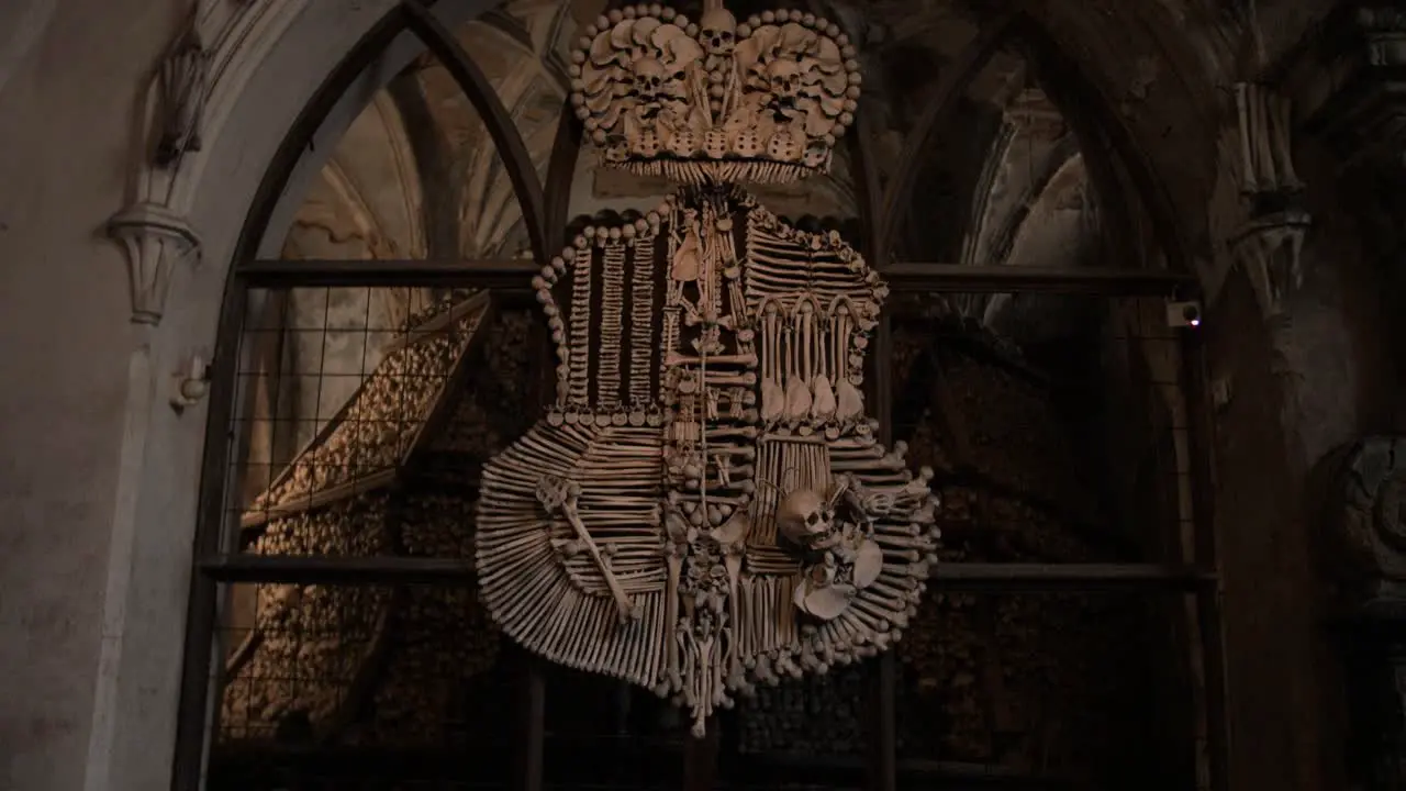 Push in shot towards coat of arms made from human bones skull remains in spook Sedlec Ossuary catholic chapel in Czech republic