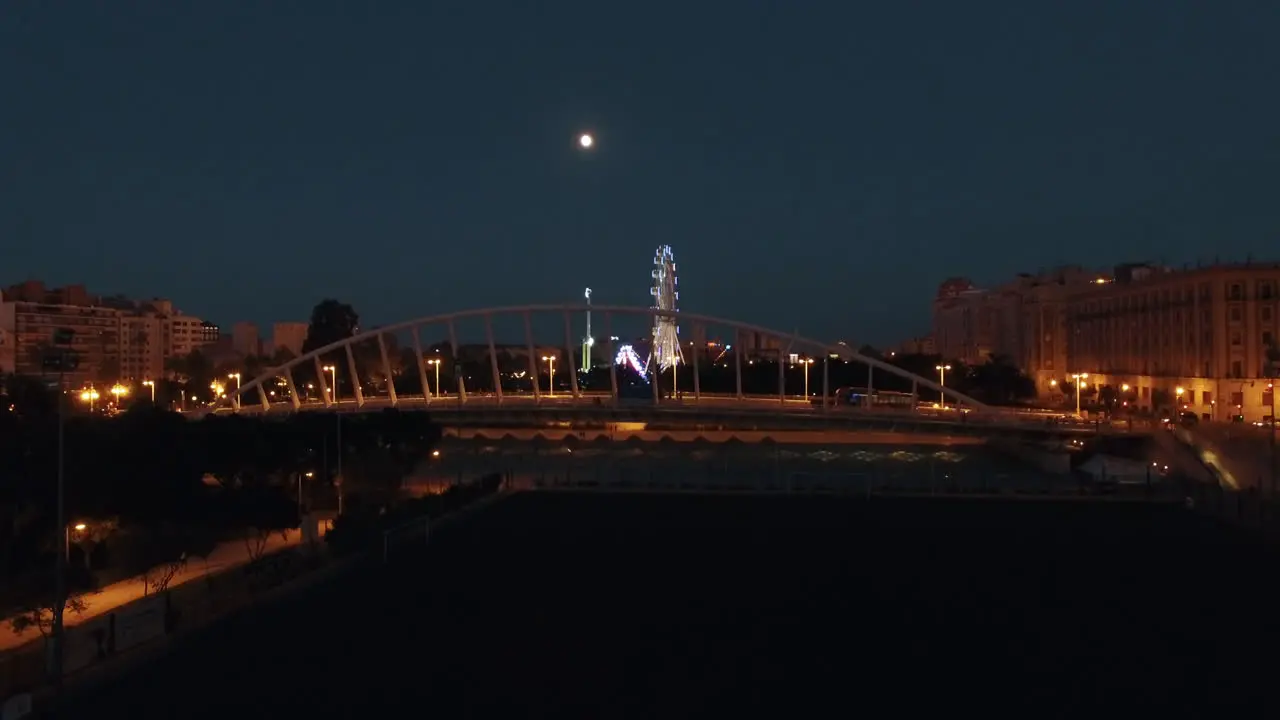 Aerial night view of lighted ferris wheel and bridge against sky with moon Valencia Spain