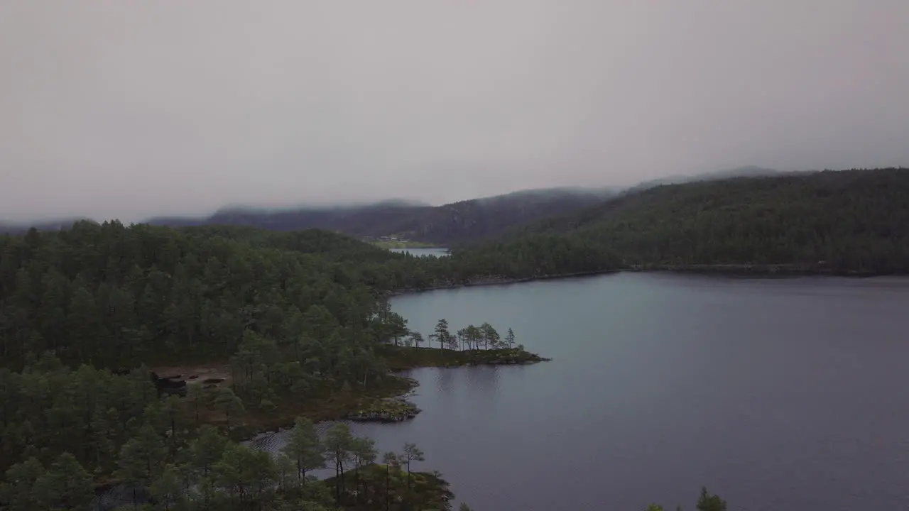 Drone shot flying over a lake and forest in Norway covered in fog and mist