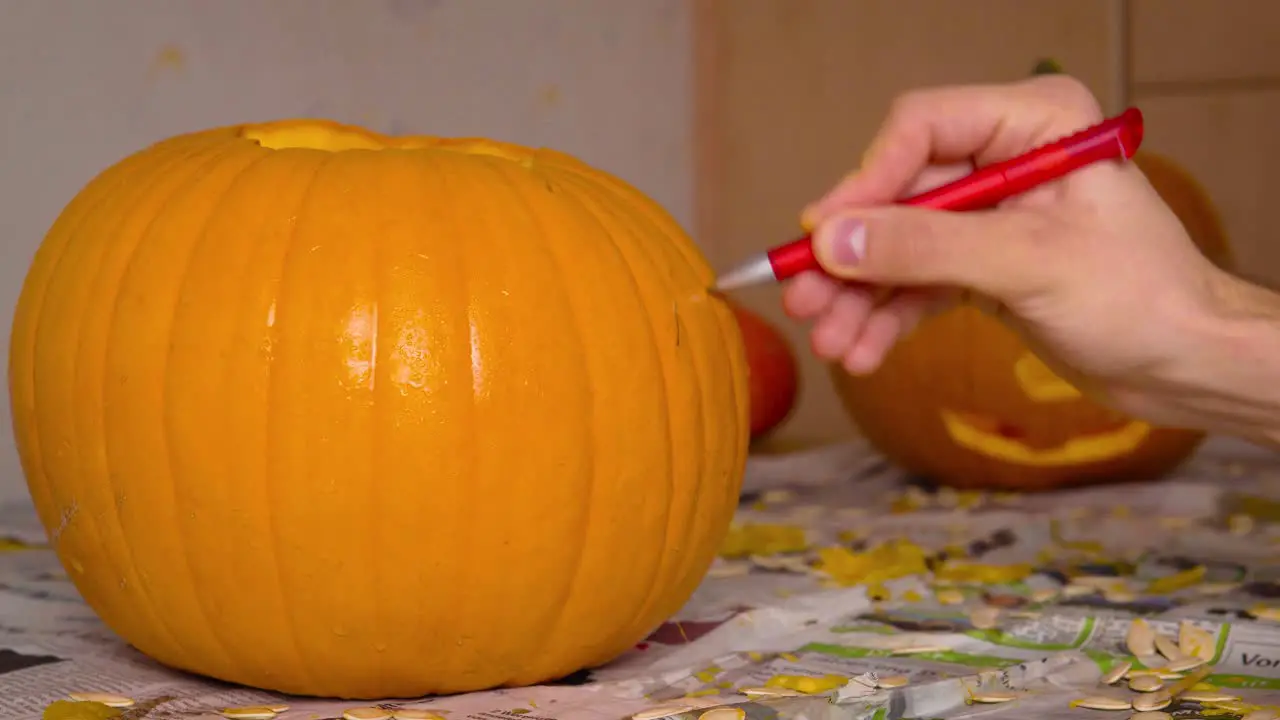 Pumpkin Carvin Male Drawing Creepy Face of Jack O'Lantern onto Pumpkin with Pen getting ready to carve Halloween decoration