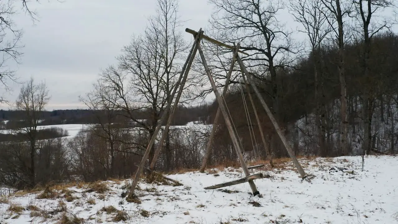 Old wooden swing near hillside move in wind overcast and snowy winter day