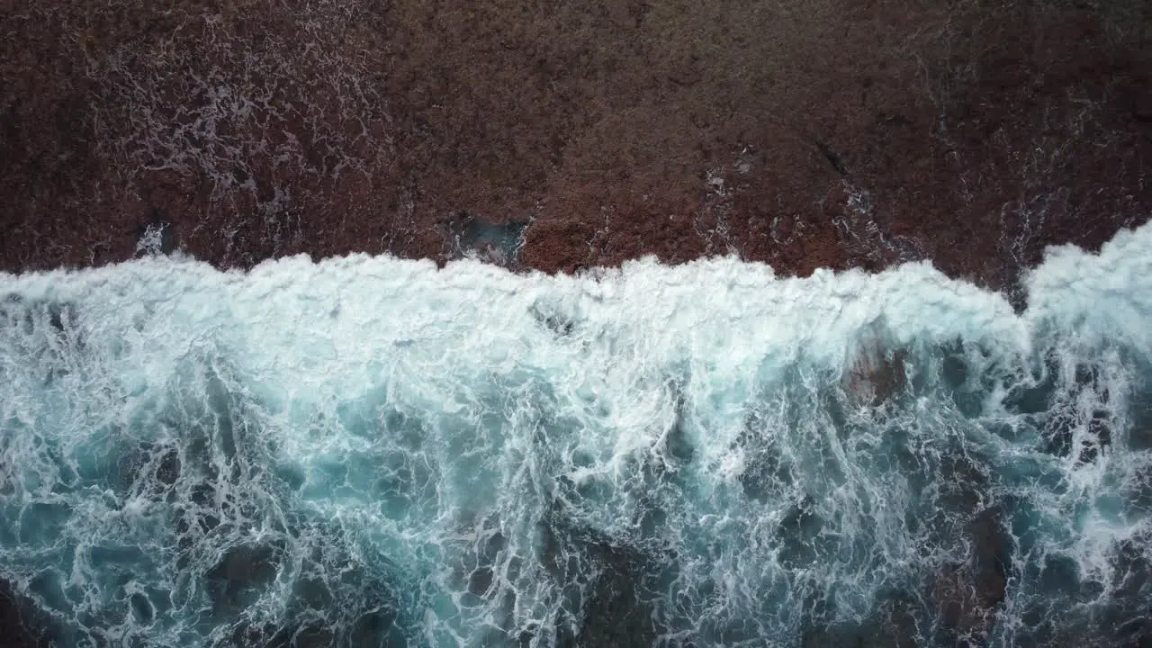 Rising bird's eye view of ocean waves crashing against Maré Island coast