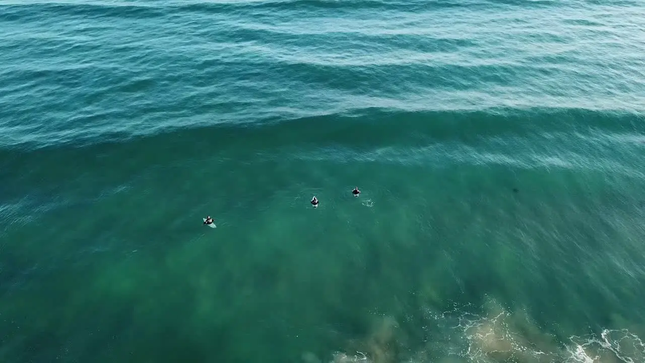 Drone aerial of surfers trying to catch a wave on a blue ocean beach Great Ocean Road