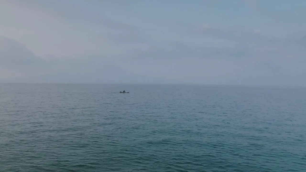 Static footage in the morning over Lake Atitlan in Guatemala with a fisherman rowing his boat across the waters