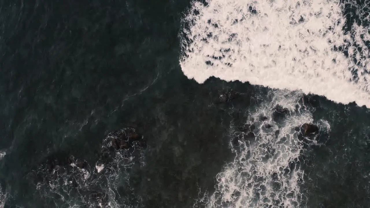 Breathtaking top aerial view of dark blue ocean and giant waves crashing at rocky cliff with splashing and white foam