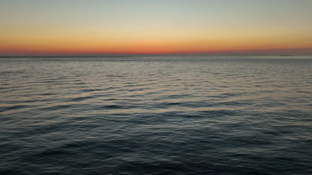 Aerial shot pulling up and away from the sun setting with a warm glow over the ocean