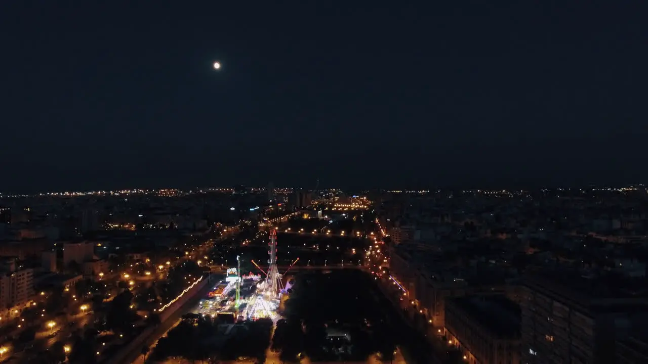 Aerial night view of lighted ferris wheel in amusement park against sky with moon Valencia Spain