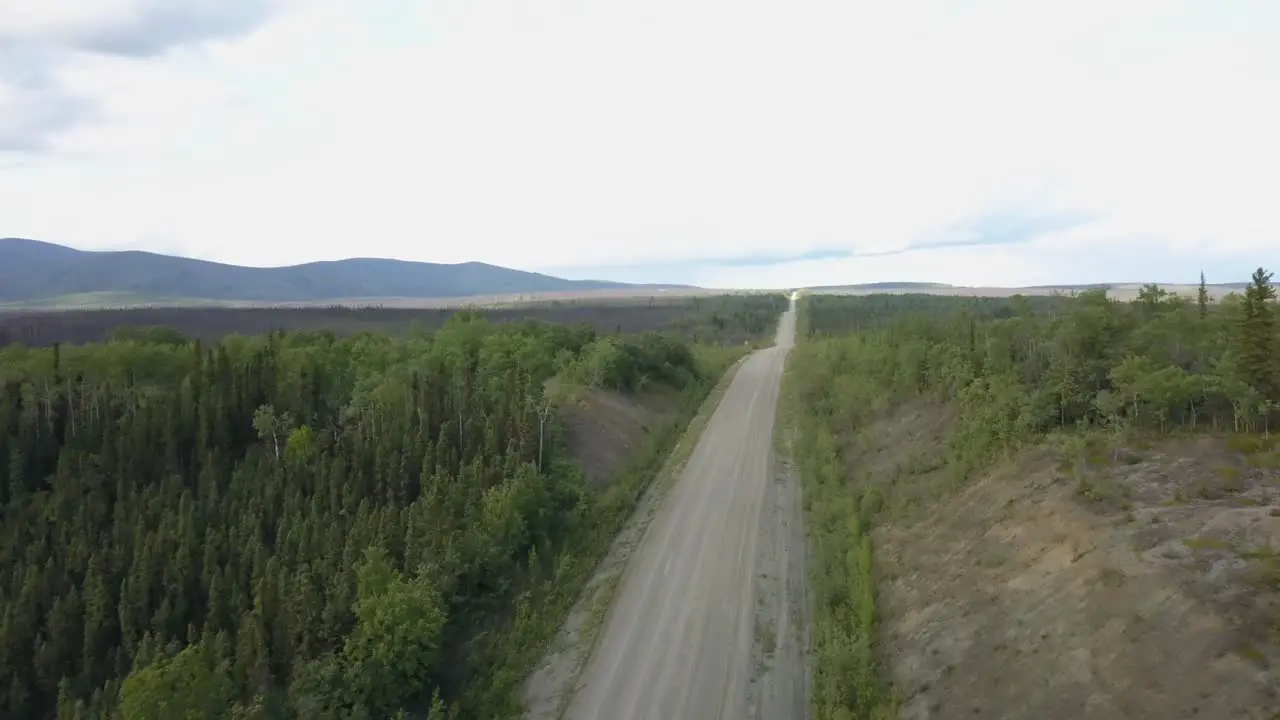 Fast moving aerial shot of rough roads in the countryside mountain range and grass in the background on Alaskan highway