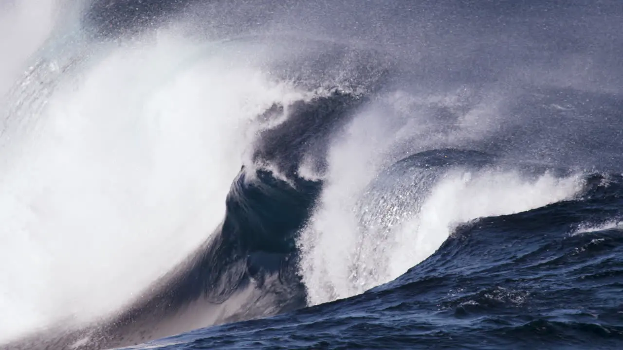 A glassy wave surges along a shallow rock shelf in slow motion while the offshore winds blow spray back up the wave face