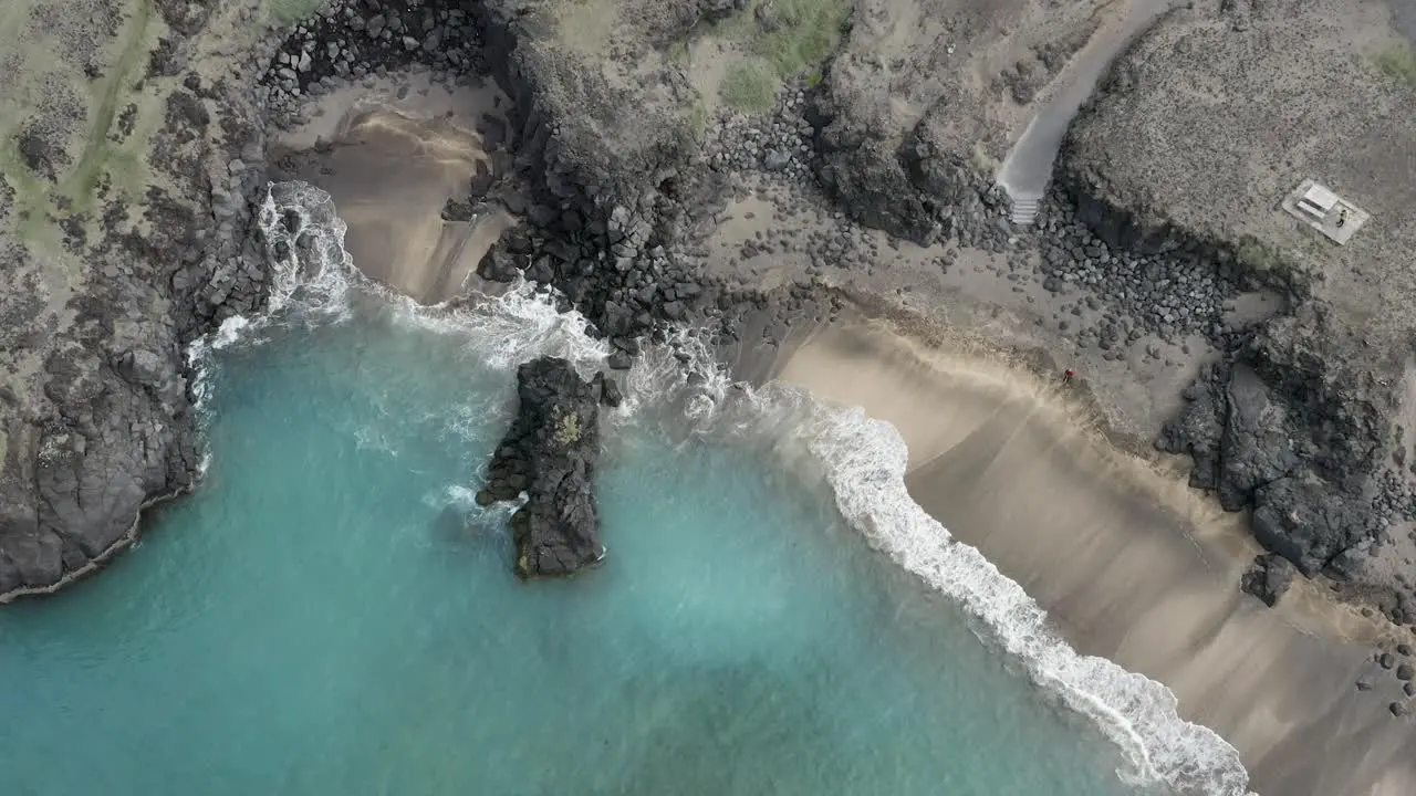 Aerial of famous Skardsvik beach with turquoise water and rocky cliff in Iceland