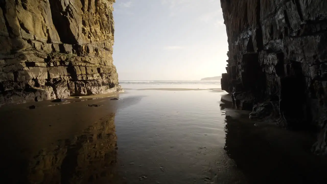 A huge sea cave with tide water coming through during sunset by the ocean with light reflected on the water above the sand