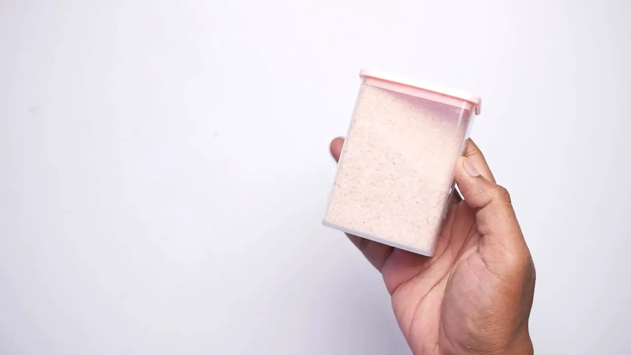 Raw whole dried pink himalayan salt in a container on white 