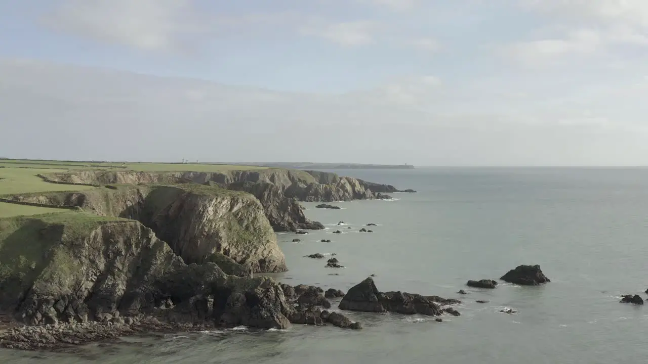 Trucking aerial flight from ocean to tall steep green Irish sea cliffs