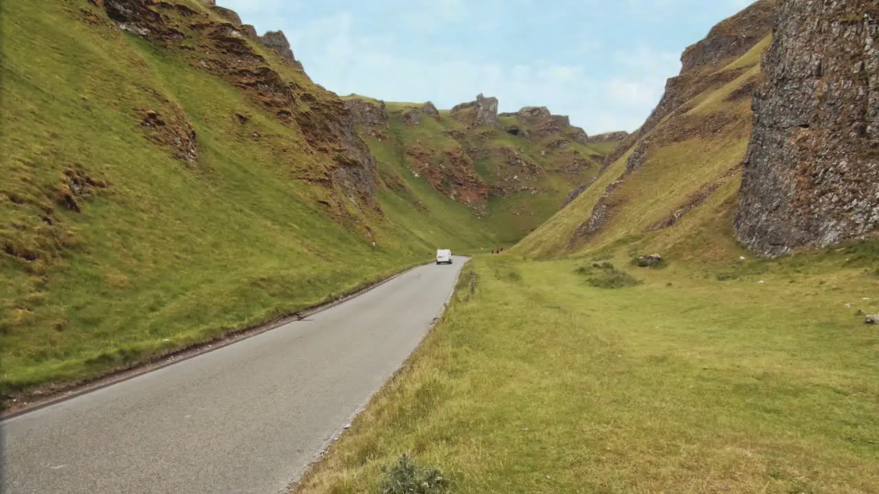 Timelapse of vehicles driving on a small road through Winnats Pass with hikers walking up the limestone hills