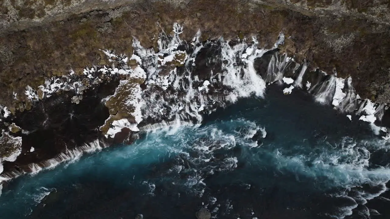 Aerial view rising away from the snowy Hraunfossar waterfall in cloudy Iceland