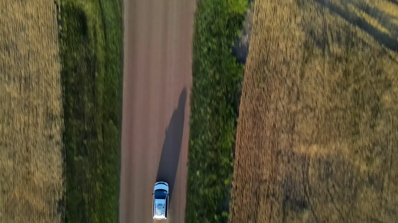 Aerial vertical shot of minivan driving along dusty gravel road in rural Alberta Canada