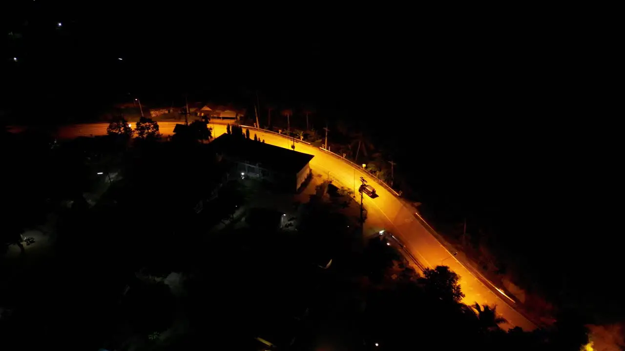 Aerial drone shot of a car driving down an empty road at night in a rural area with yellow street lights