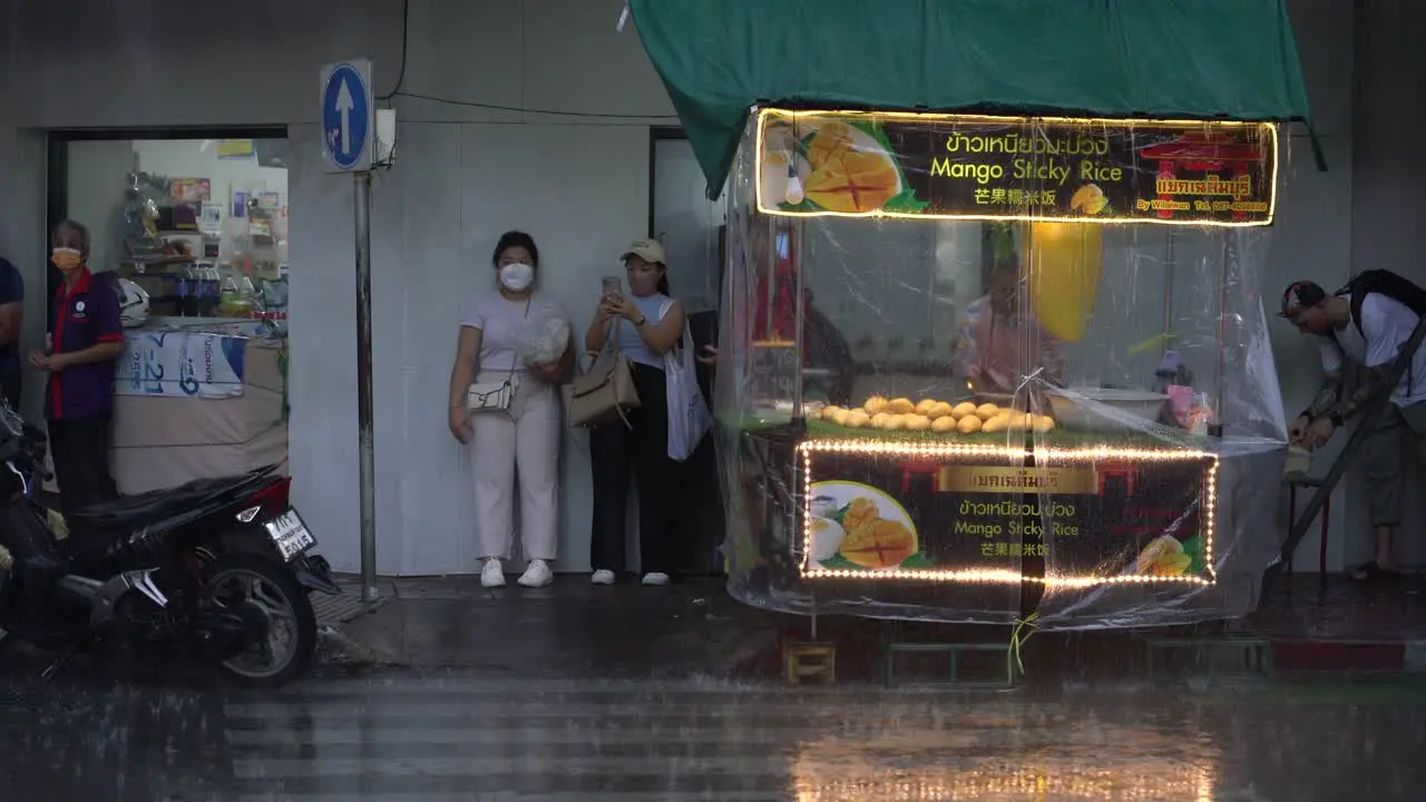 People waiting for rain to stop next to mango sticky rice stall