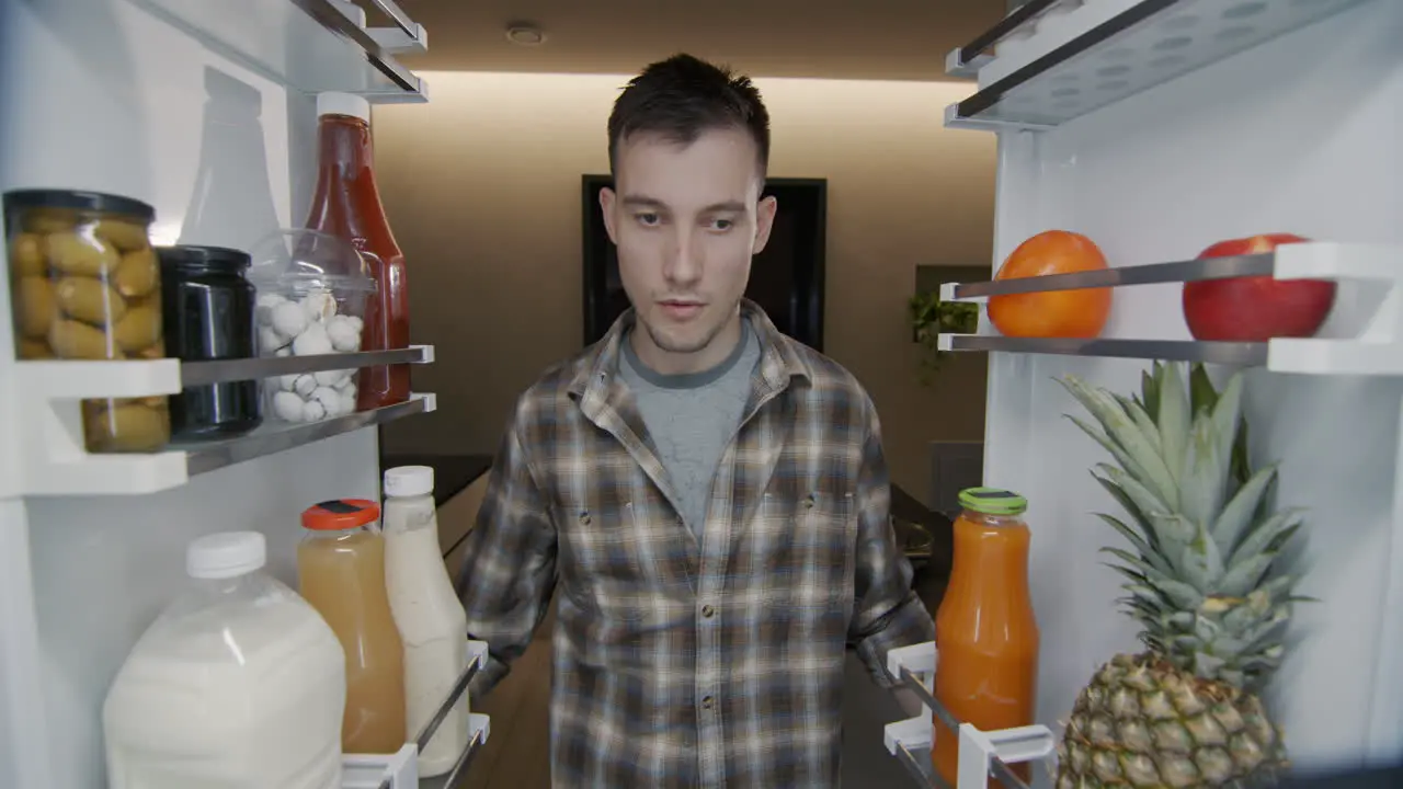 A man takes a red apple from the refrigerator Light snack and healthy eating concept