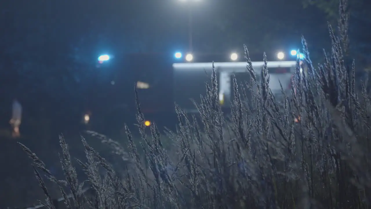 Fire Truck with Blinking Emergency Lights Seen Through Grass at Night