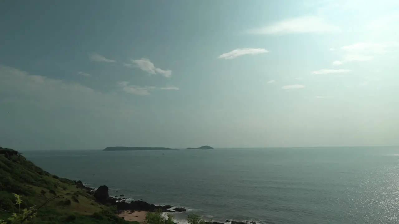 Static cinematic timelapse shot of a large lake with calm waters with lake islands and a shore with rocks in the foreground while the clouds pass by on the horizon