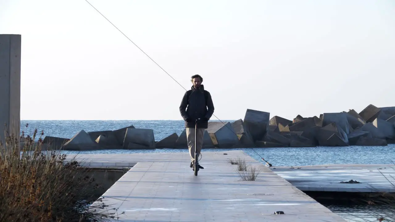 Man riding elecric scooter on ocean boardwalk toward camera in Barcelona Spain