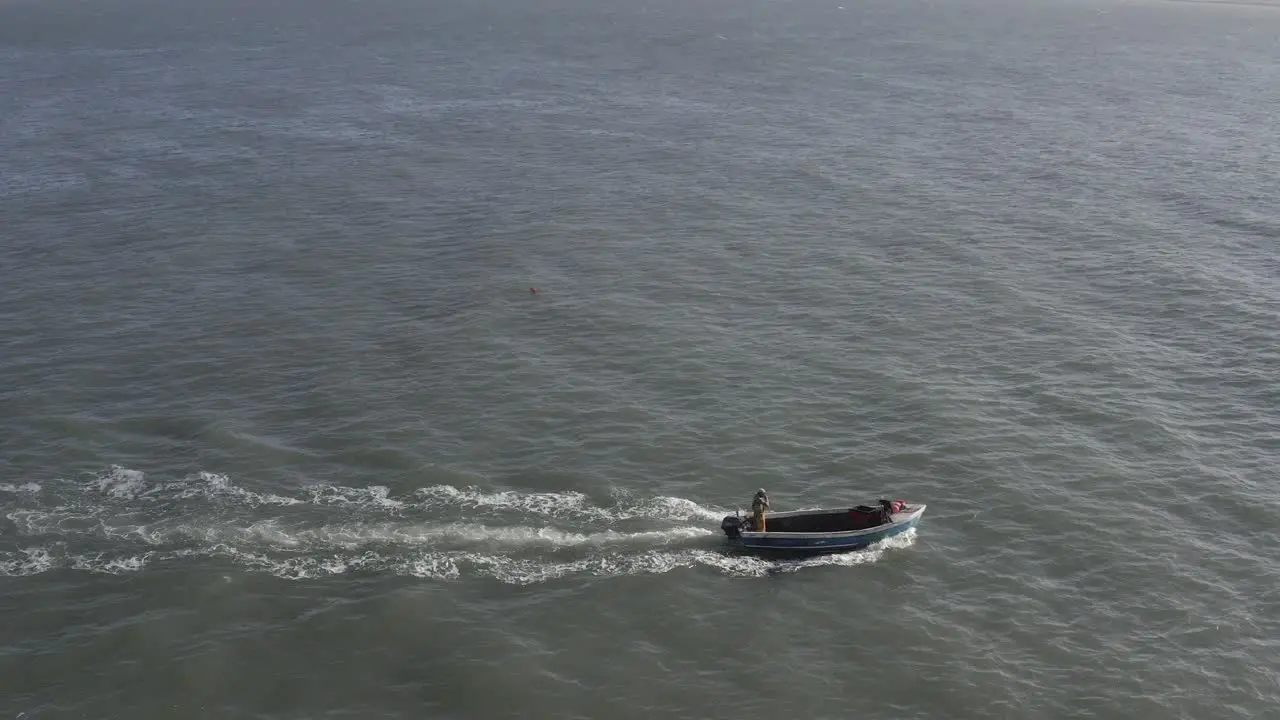 Small open lobster boat crosses frame left to right on open water