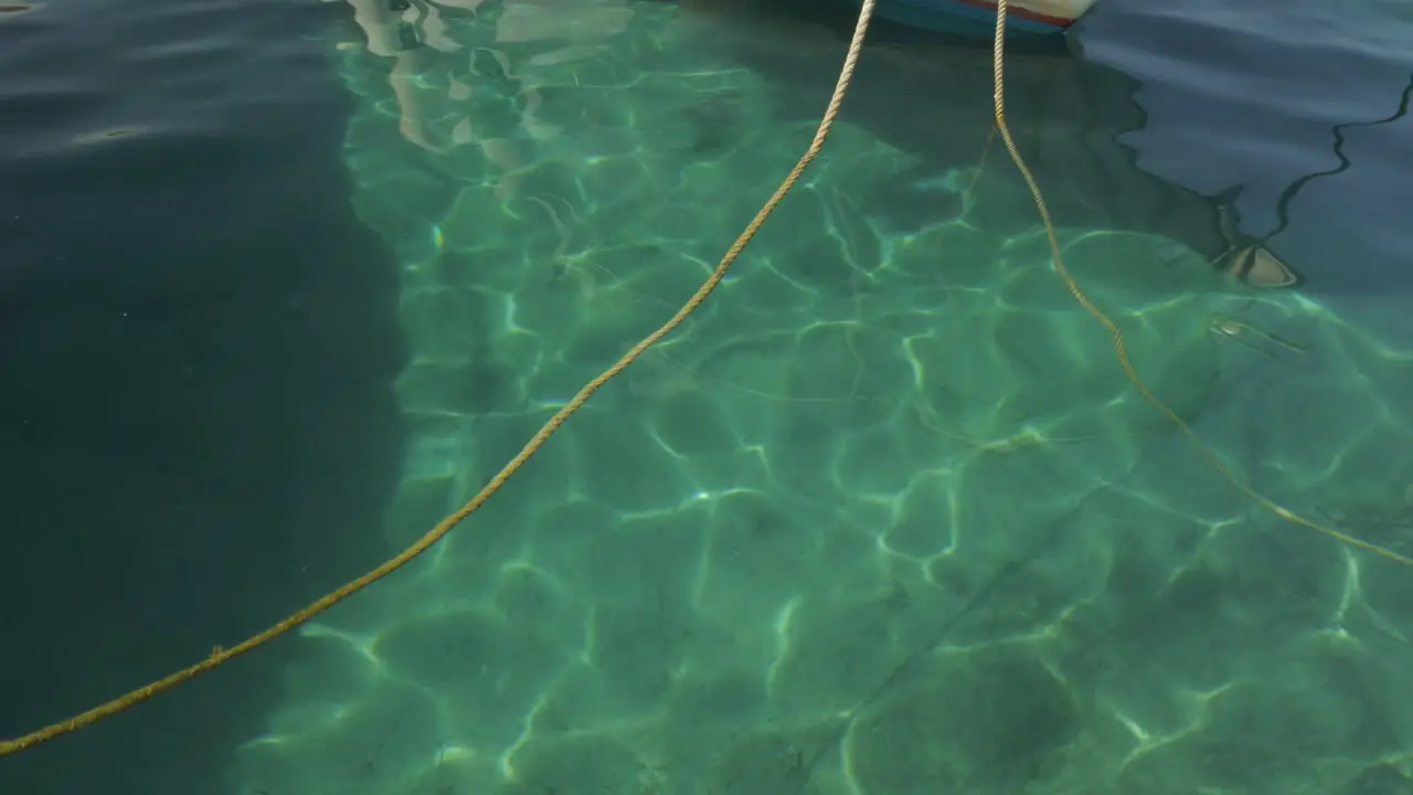 Close up of the sunlight reflection in the green cristal sea near à small fishing boat anchored at the port of Egliali in Greece