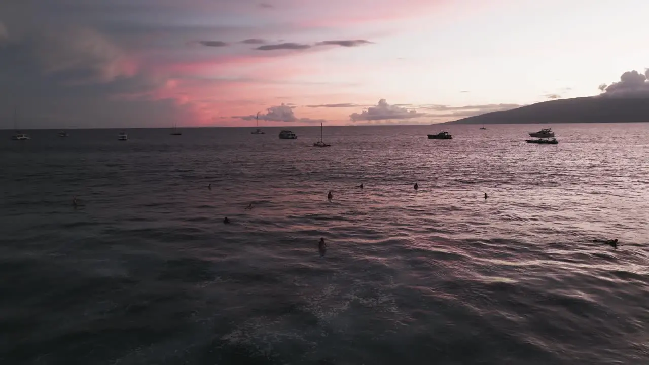 Surfers and boaters enjoying ocean view of red pink sunset Lahaina Maui Hawaii