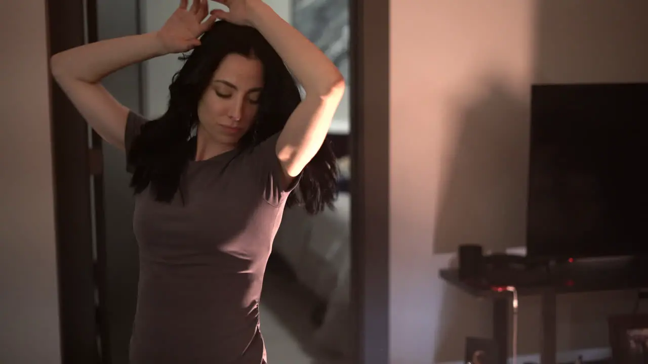 Young attractive woman having fun dancing and singing in her apartment alone looking straight into the camera gimbal shot