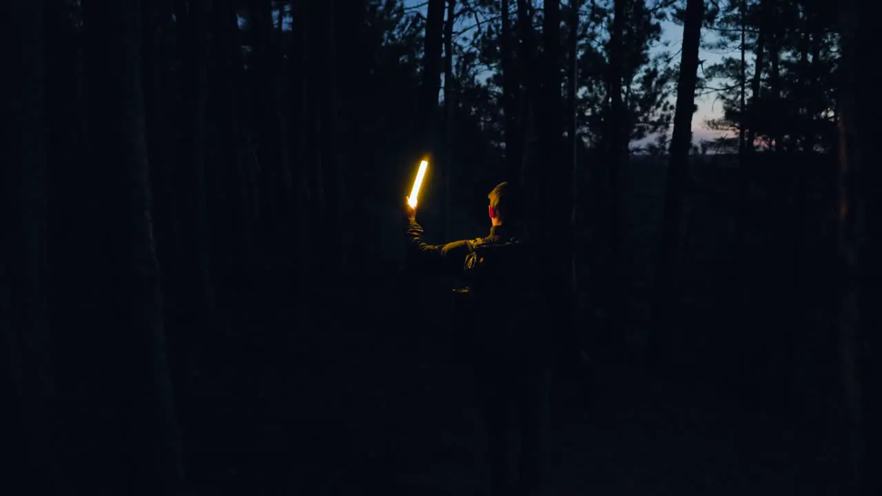 adventurer with backpack and torch light walks though dark forest searching the darkness at night