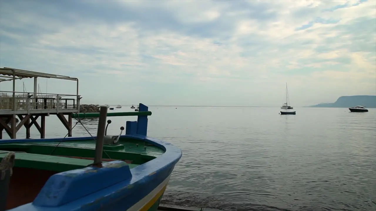 Slow pullback beside colorful wooden fishing boat on shore of calm bay