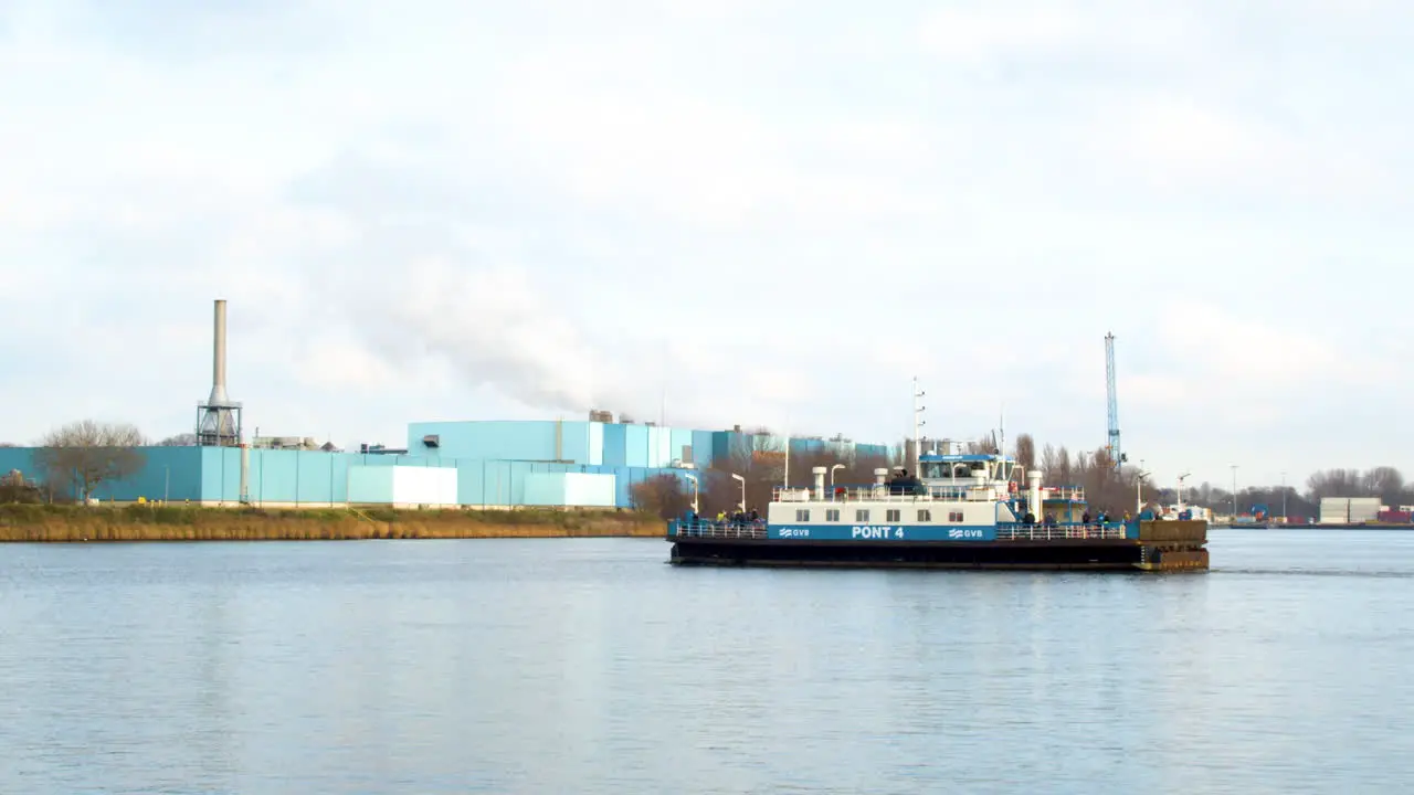 Amsterdam ferry crossing river with a smoking industrial building in the background