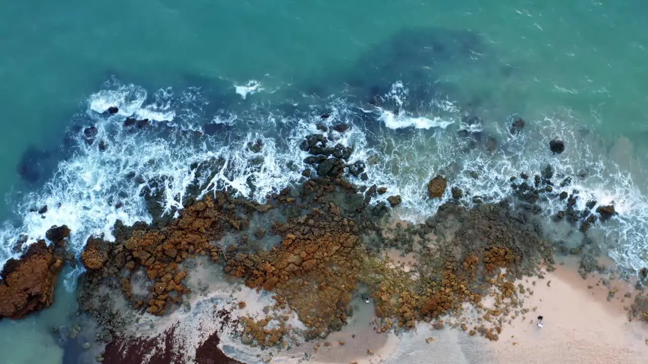 Beautiful lowering bird's eye view of ocean waves hitting rocks on the shore of a tropical Northern Brazil beach named Tabatinga with blue water and golden sand near Joao Pessoa on a warm summer day