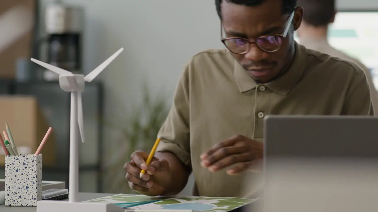 Hombre De Negocios Que Usa Una Computadora Portátil Sentada En La Mesa Con Un Modelo De Molino De Viento En La Oficina 2