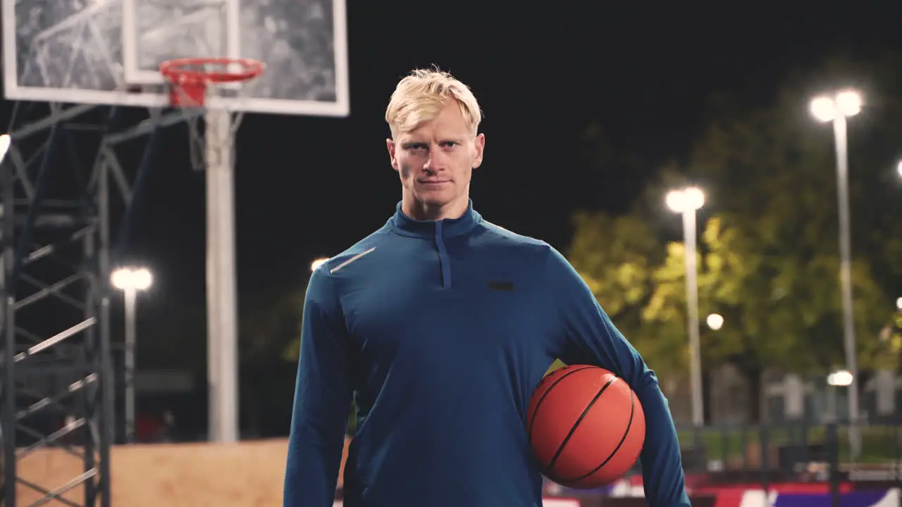 Retrato De Un Jugador De Baloncesto Confiado Sosteniendo La Pelota Y Mirando La Cámara Mientras Está De Pie En Una Cancha Al Aire Libre Por La Noche 1